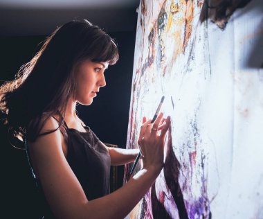 Stüdyoda iş yerinde genç sanatçı. Arka planda büyük tuval