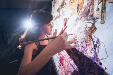 Stüdyoda iş yerinde genç sanatçı. Arka planda büyük tuval