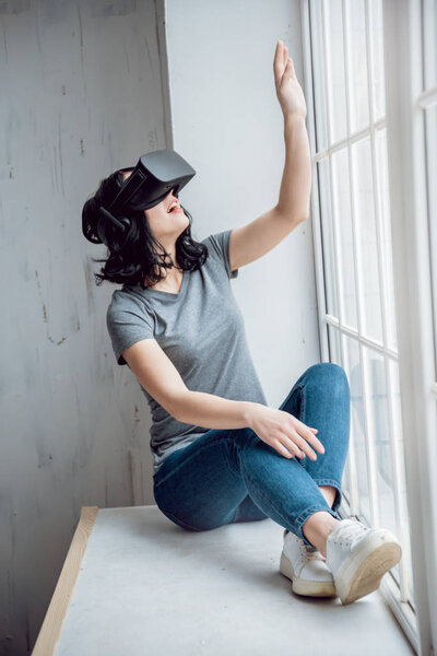Young girl wearing virtual reality goggles sitting by the window