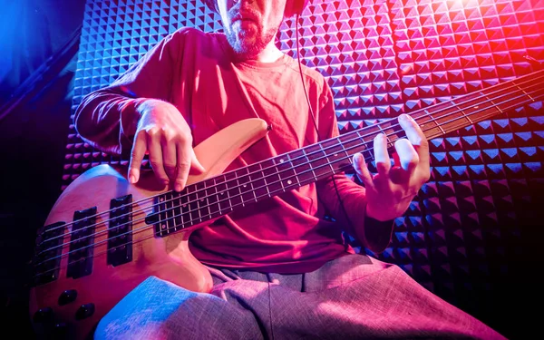 Young man playing on the bass guitar in sound recording studio. Modern background