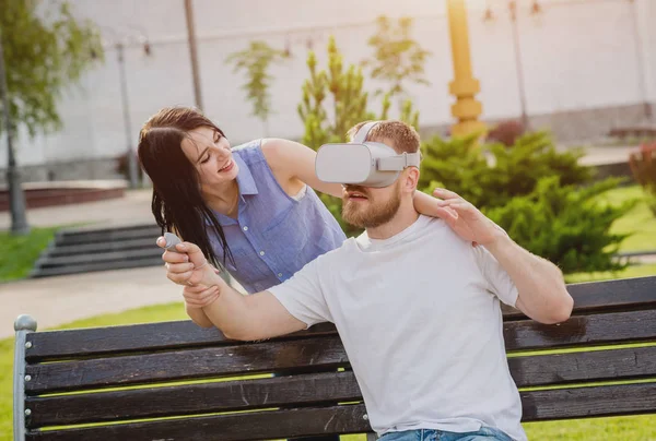 Young caucasian couple plays a game using virtual reality glasses on the street. VR headset.