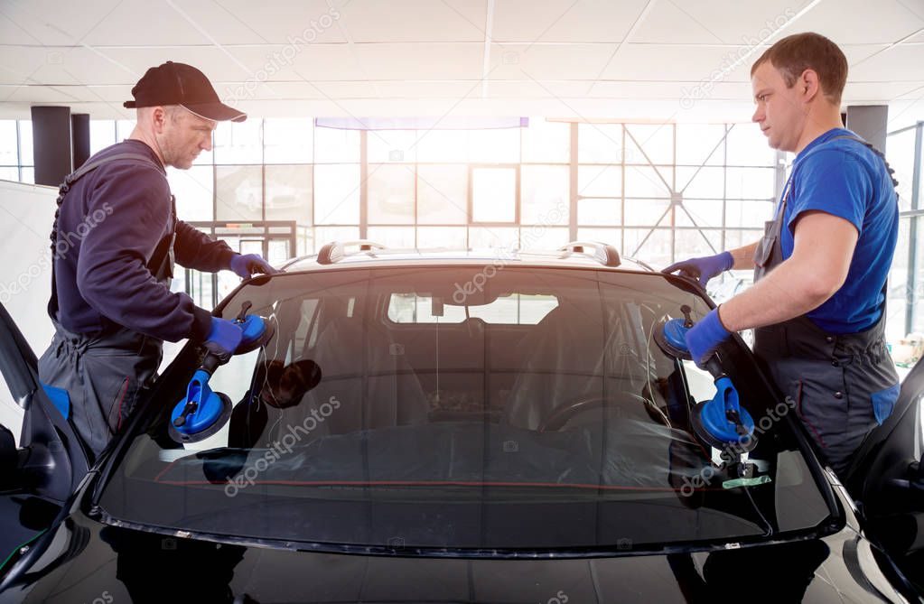 Automobile special workers replacing windscreen of car in auto service station garage