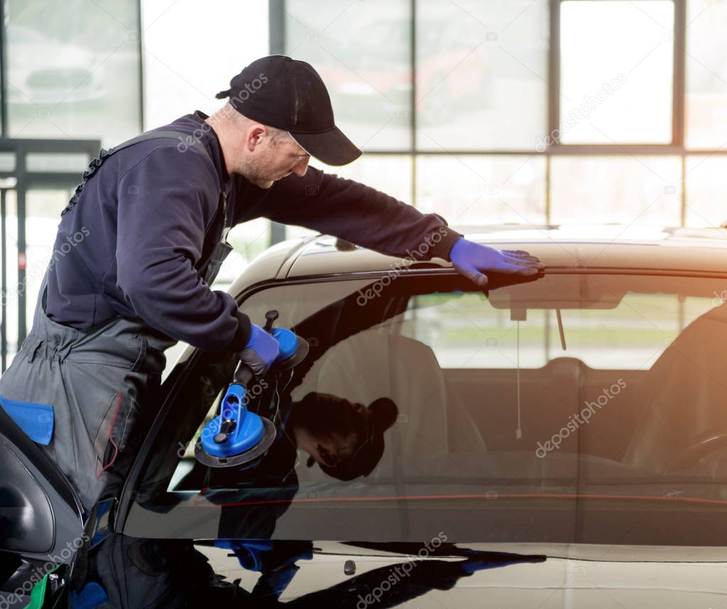Automobile special worker replacing windscreen or windshield of a car in auto service station garage. Background