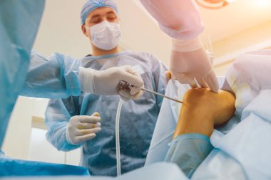 Arthroscope surgery. Orthopedic surgeons in teamwork in the operating room with modern arthroscopic tools. Knee surgery. Hospital background clipart