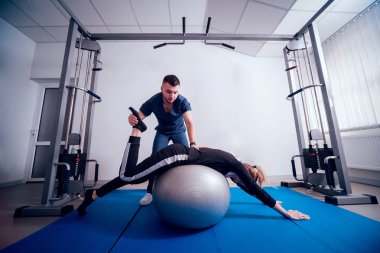 Rehabilitasyon kavramı. Güzel genç kadın fizyoterapist gözetiminde topu ile yapıyor. Egzersiz tedavisi