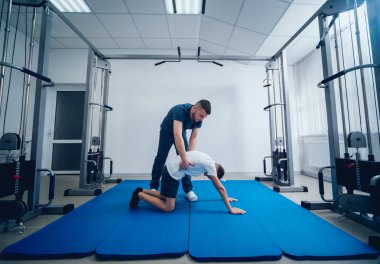 Rehabilitasyon kavramı. Genç çocuk mat fizyoterapist gözetiminde egzersizleri yapıyor. Egzersiz tedavisi