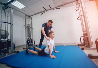 Rehabilitasyon kavramı. Genç çocuk mat fizyoterapist gözetiminde egzersizleri yapıyor. Egzersiz tedavisi