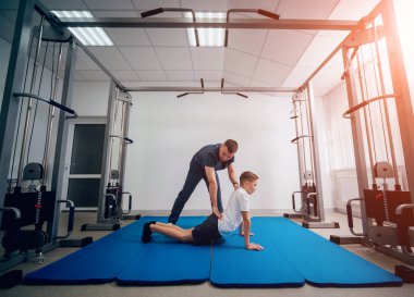 Rehabilitasyon kavramı. Genç çocuk mat fizyoterapist gözetiminde egzersizleri yapıyor. Egzersiz tedavisi