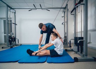 Rehabilitasyon kavramı. Genç çocuk mat fizyoterapist gözetiminde egzersizleri yapıyor. Egzersiz tedavisi