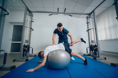 Rehabilitasyon kavramı. Genç çocuk topu fizyoterapist gözetiminde ile yapıyor. Egzersiz tedavisi