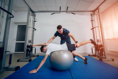 Rehabilitasyon kavramı. Genç çocuk topu fizyoterapist gözetiminde ile yapıyor. Egzersiz tedavisi