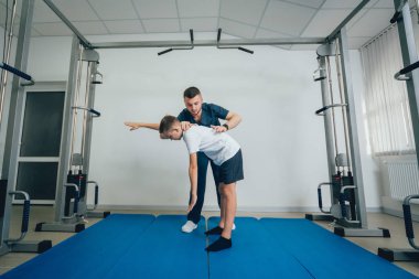 Rehabilitasyon kavramı. Genç çocuk mat fizyoterapist gözetiminde egzersizleri yapıyor. Egzersiz tedavisi