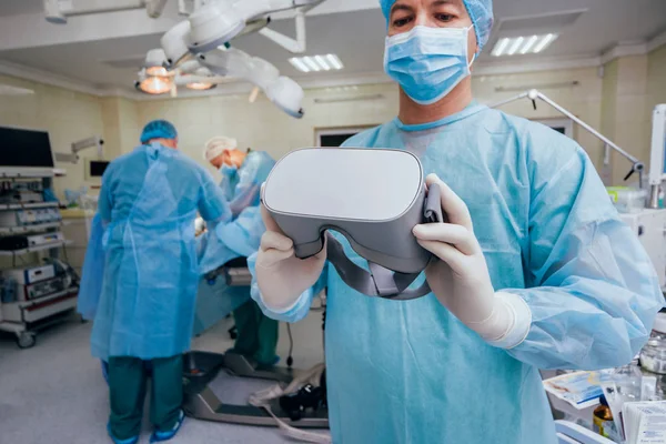 Doctor in a surgical room with virtual reality glasses on the background of the real operation. Modern technologies