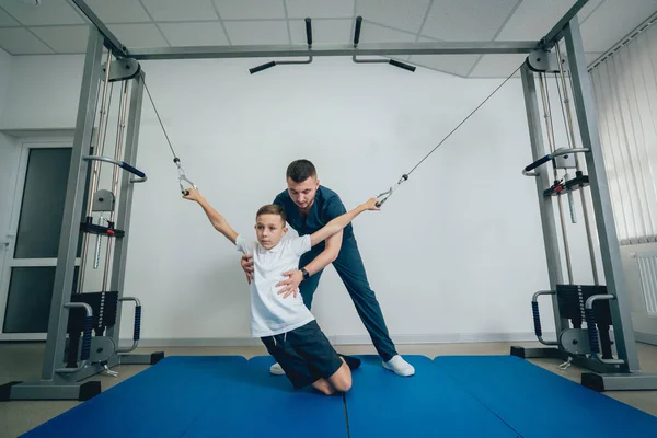 Rehabilitasyon kavramı. Genç çocuk mat fizyoterapist gözetiminde egzersizleri yapıyor. Egzersiz tedavisi