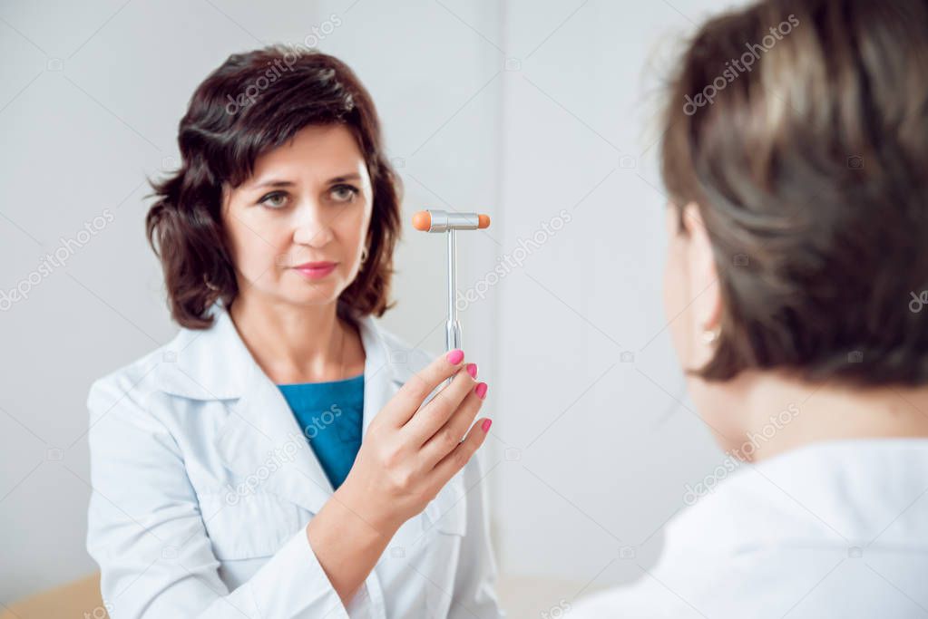 Neurological examination. The neurologist testing reflexes on a female patient using a hammer. Diagnostic, healthcare, medical service