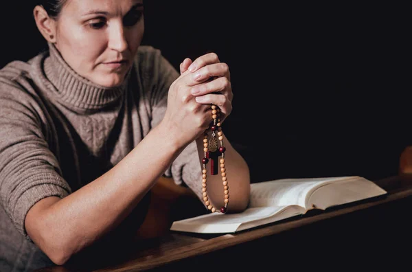 Christian woman praying in church. Hands crossed and Holy Bible on wooden desk. Background