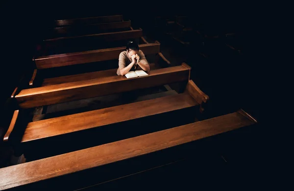 Christian woman praying in church. Hands crossed and Holy Bible on wooden desk. Background