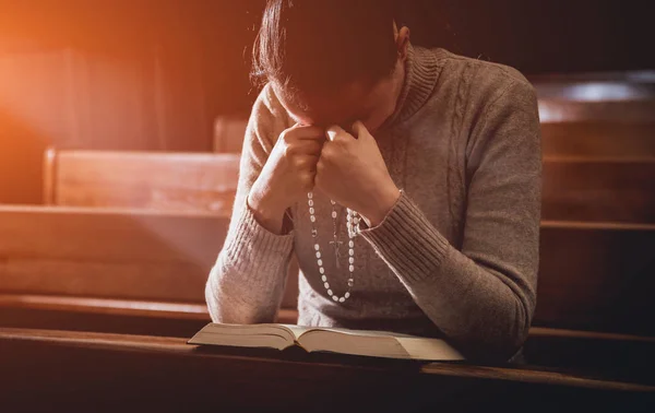 Christian woman praying in church. Hands crossed and Holy Bible on wooden desk. Background