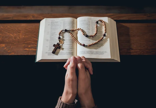 Christian woman praying in church. Hands crossed and Holy Bible on wooden desk. Background