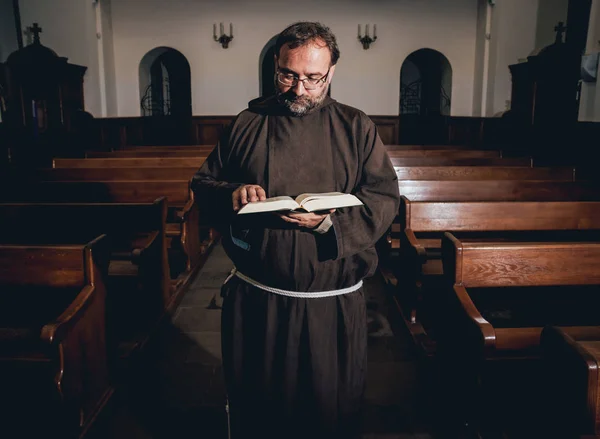A monk in robes with holy bible in their hands praying in the church. Background