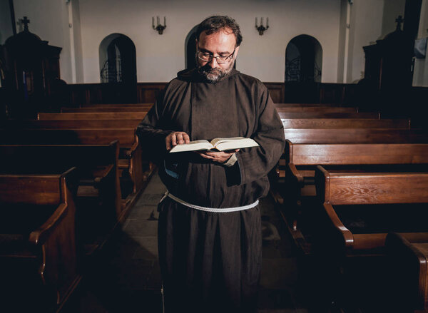 A monk in robes with holy bible in their hands praying in the church. Background