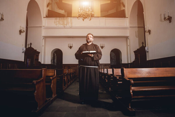 A monk in robes with holy bible in their hands praying in the church. Background