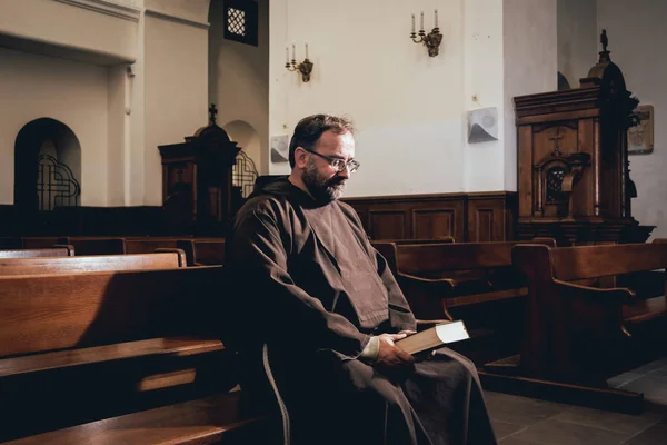 A monk in robes with holy bible in their hands praying in the church. Background