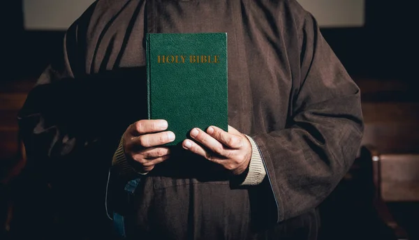 A monk in robes with holy bible in their hands praying in the church. Background