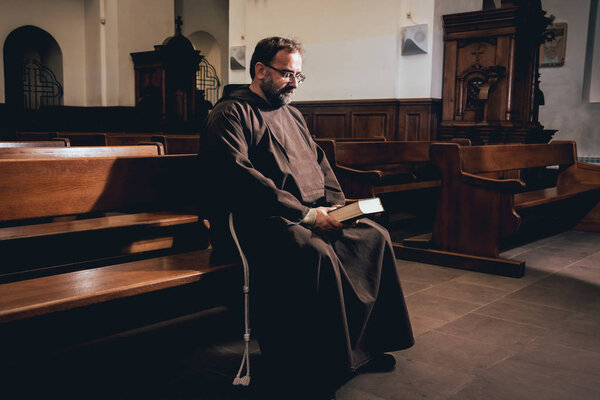 A monk in robes with holy bible in their hands praying in the church. Background