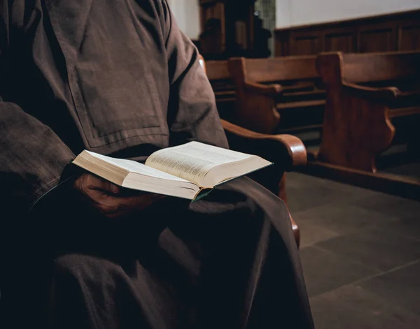 A monk in robes with holy bible in their hands praying in the church. Background