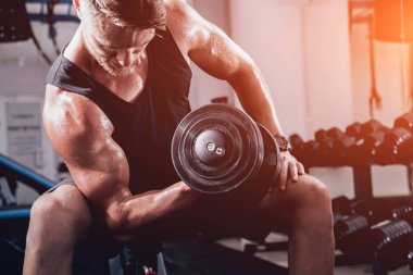 Yakışıklı kaslı adam spor salonunda dambıllarla çalışıyor.