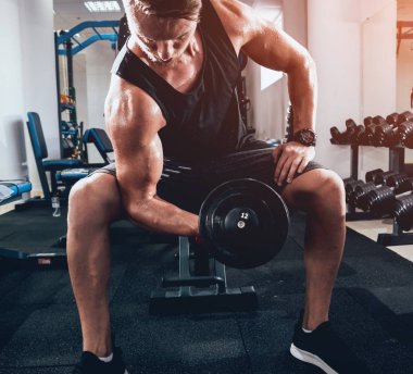 Yakışıklı kaslı adam spor salonunda dambıllarla çalışıyor.