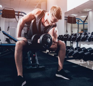 Yakışıklı kaslı adam spor salonunda dambıllarla çalışıyor.