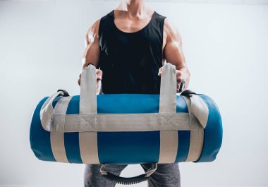 Gri arka plan, kum torbası ile eğitim atletik genç adam. Eğitim çapraz. Fitness kavramı.