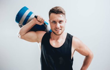 Atletik genç adam gri arka planda kum torbalarıyla antrenman yapıyor.