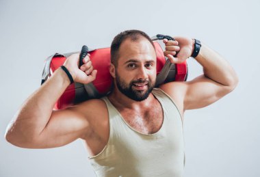 Atletik genç adam gri arka planda kum torbalarıyla antrenman yapıyor.