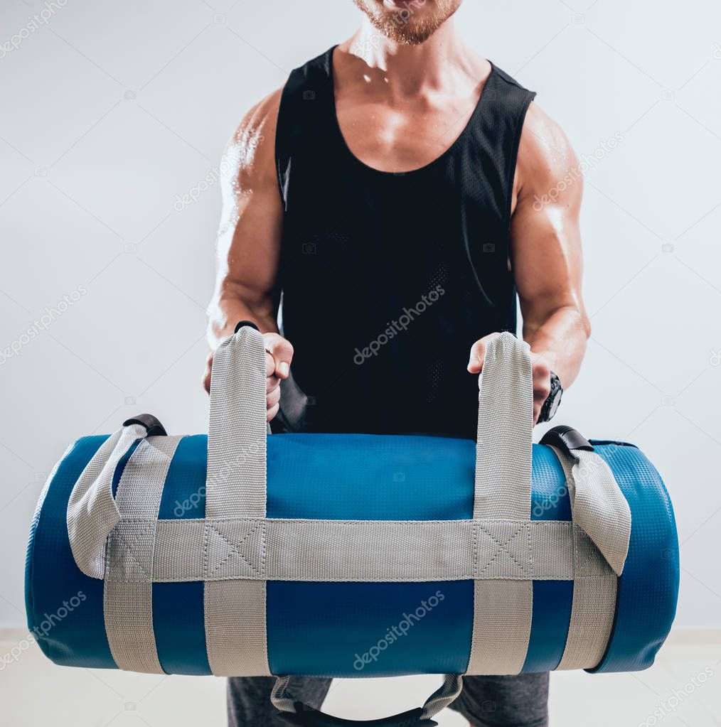 Athletic young man training with sandbags at gray background. Cross training. Fitness concept.