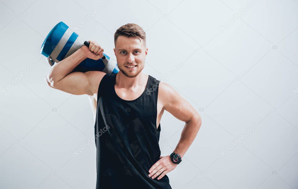Athletic young man training with sandbags at gray background