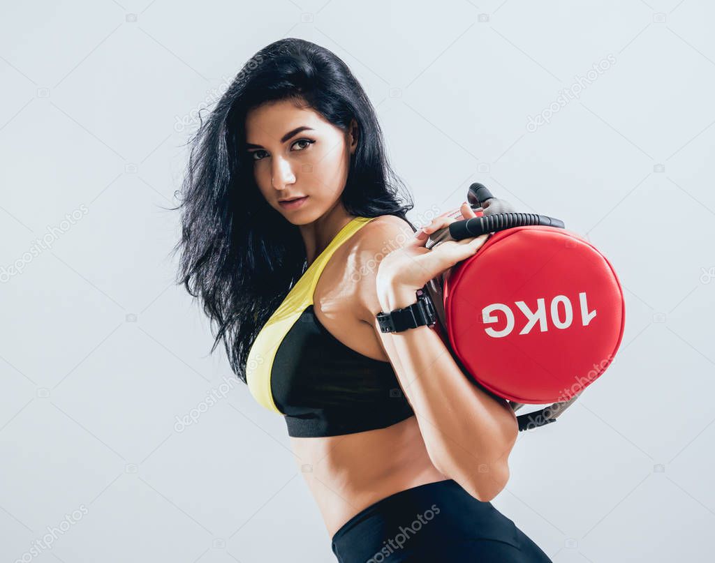 Athletic young woman training with sandbags at gray background. Cross center. Fitness concept.