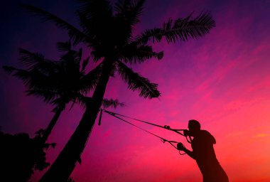 Atlet palmiye ağacında sabit olan Fitness kayışları ile plajda egzersizleri gerçekleştirir. Günbatımı. Arka plan