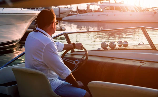 Young man on sailing yacht holding hands on steering wheel