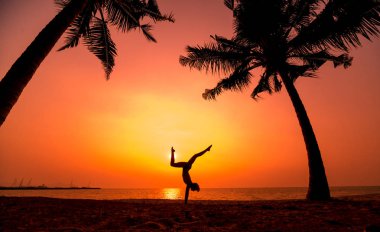 Güzel ve genç birbayan practic yoga sahilde. Sabah egzersiz. Güneş doğuyor. Avuç içi arka plan