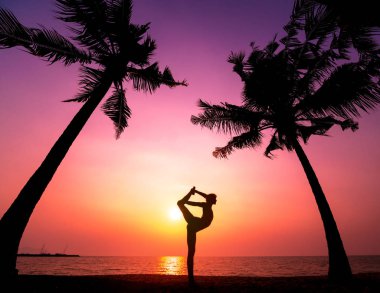 Güzel ve genç birbayan practic yoga sahilde. Sabah egzersiz. Güneş doğuyor. Avuç içi arka plan