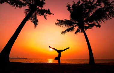 Güzel ve genç birbayan practic yoga sahilde. Sabah egzersiz. Güneş doğuyor. Avuç içi arka plan