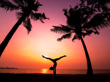 Güzel ve genç birbayan practic yoga sahilde. Sabah egzersiz. Güneş doğuyor. Avuç içi arka plan