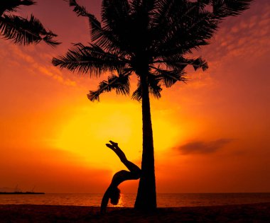 Güzel ve genç birbayan practic yoga sahilde. Sabah egzersiz. Güneş doğuyor. Avuç içi arka plan