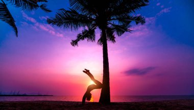 Güzel ve genç birbayan practic yoga sahilde. Sabah egzersiz. Güneş doğuyor. Avuç içi arka plan