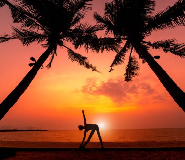 Güzel ve genç birbayan practic yoga sahilde. Sabah egzersiz. Güneş doğuyor. Avuç içi arka plan