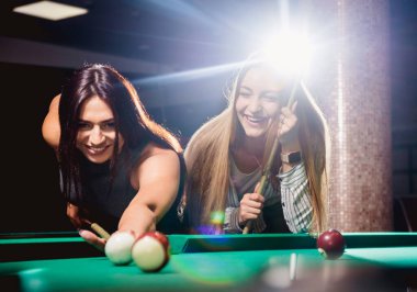 Bilardo oynayan iki genç kadın. Arka planda bilardo odası..
