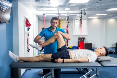 Rehabilitasyon terapisi. Rehabilitasyon merkezinde genç bir erkek hastayla çalışan fizyoterapist.